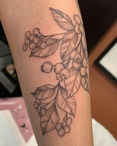 a tattoo on the leg of a woman with berries and leaves around her arm,