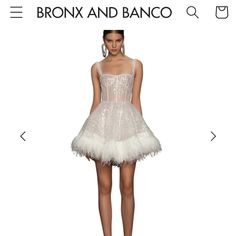 a woman in a short white dress with feathers on the skirt and heels, standing next to an advertisement for bronx and banco