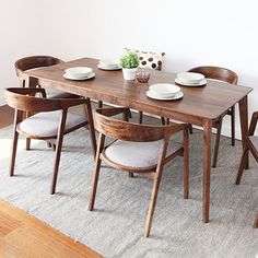 a wooden table with white plates and bowls on it in front of a wall mounted plant