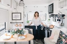 a woman standing in the kitchen area of a camper with flowers on the table