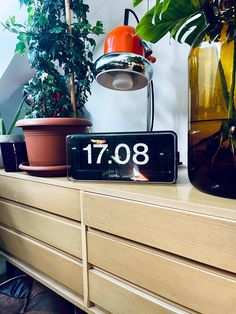 an alarm clock sitting on top of a dresser next to potted plants and a lamp