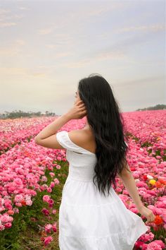 a woman in a white dress is standing in a field of pink and yellow flowers