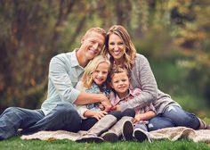 a family sitting on a blanket together in the grass with trees in the back ground