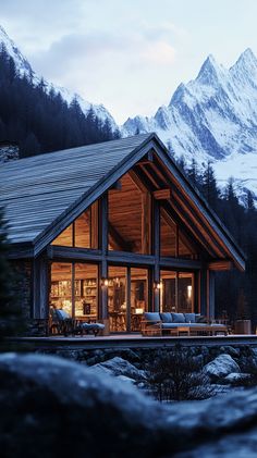 a cabin with mountains in the background at night, lit up by lights on windows