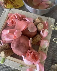 some pink flowers and wine corks on a wooden tray next to a metal bowl