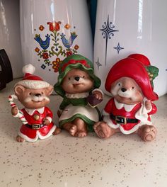 three ceramic garden gnomes sitting next to each other on a counter with white vases behind them