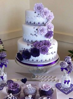 a wedding cake and cupcakes on a table with purple flowers in the middle