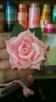 a person holding a pink rose in front of some spools of colored thread