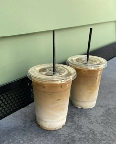 two iced coffees sitting on the ground next to each other with black straws