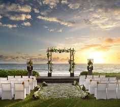 an outdoor ceremony set up with white chairs and greenery on the lawn, overlooking the ocean