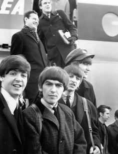 black and white photograph of the beatles in front of an airplane with people standing around