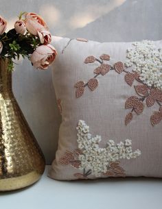 a gold vase with flowers next to a pillow on a white tablecloth covered shelf