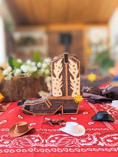 a wooden cowboy boot sitting on top of a red bandanna table cloth next to other items