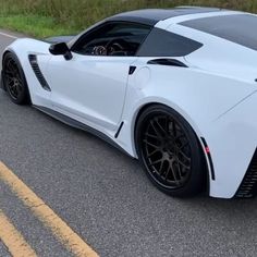 a white sports car is driving down the road with its hood up and black wheels