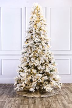 a white christmas tree in a room with wood flooring and wooden walls, decorated with gold trimmings