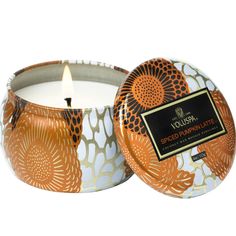 an orange and white candle in a tin with a flower design on the lid that says vodoui