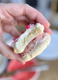 a hand holding a half eaten doughnut with white frosting and sprinkles