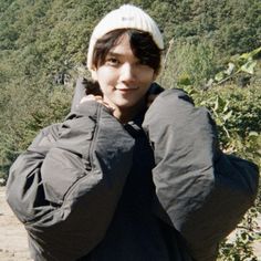 a young man wearing a beanie and jacket posing for a photo in front of some trees