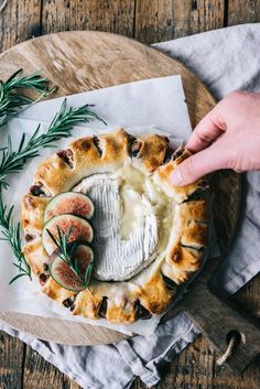 a person holding a piece of bread with cheese and figs in it on a plate