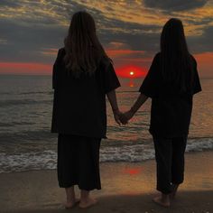 two women hold hands as the sun sets over the ocean