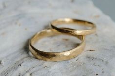 two gold wedding rings sitting on top of a rock