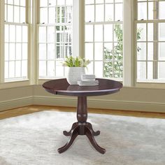 a round table with two white vases on it in front of three large windows