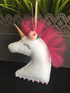 a white unicorn with pink hair and a rose on it's head sitting next to some plants