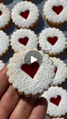 a person holding up a heart shaped cookie in front of some cookies with hearts on them