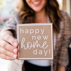 a woman holding up a card with the words happy new home day written on it