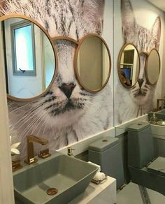 a bathroom with two sinks, mirrors and a cat mural on the wall behind it