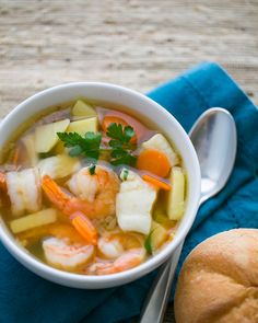 a bowl of soup with shrimp, carrots and celery next to a roll