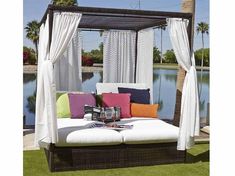 an outdoor daybed with pillows and curtains on the top, next to a lake