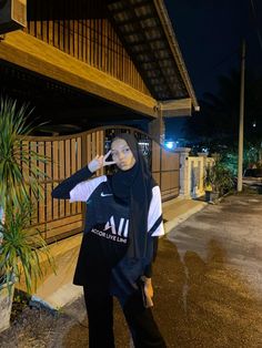 a woman in hijab standing on the street at night talking on her cell phone