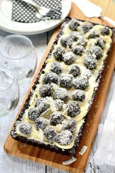 a wooden cutting board topped with a dessert covered in powdered sugar next to wine glasses