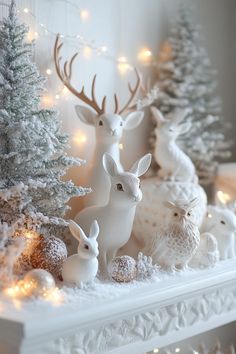 white christmas decorations with deer and rabbits on the mantel in front of lit trees