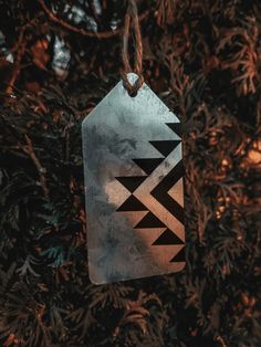 a metal tag hanging from a tree with leaves and branches in the background, that has a pattern on it