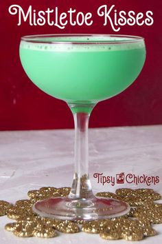 a green drink in a coupe glass with gold confetti on the rim and text overlay that says mistleto kisses