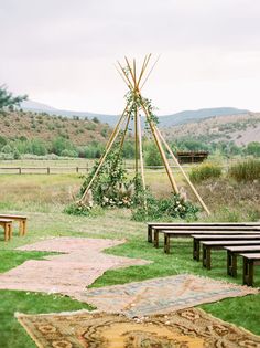 an outdoor ceremony setup with wooden benches and teepees on the grass in front of mountains