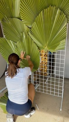 a woman is sitting on the ground working on a large green object that looks like palm leaves