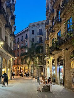 two women sitting on a bench in the middle of an empty street at night time