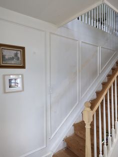 a white staircase with wooden handrails and framed pictures on the wall next to it