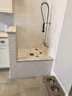 a white tiled bathroom with a stainless steel dog bowl in the middle and a shower head