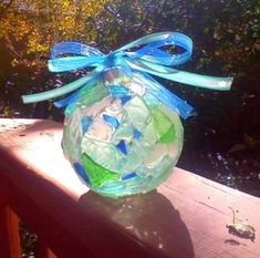 a glass vase sitting on top of a wooden table covered in sea glass and blue ribbon