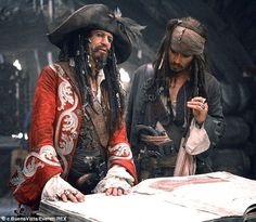 two men dressed in pirate costumes look at something on the table as they stand next to each other