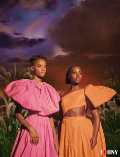 two women standing next to each other in front of a sky with clouds and grass