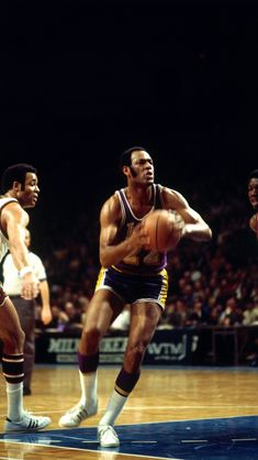 two men playing basketball on a court with people watching from the sidelines behind them