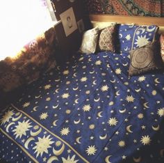 a bed covered in blue and white sheets with sun and moon designs on it, next to a window