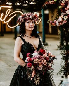 a woman in a black dress is holding a bouquet and standing under a neon sign