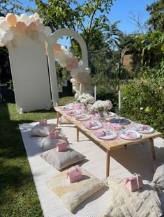 a long table set up with pink and white plates, napkins, and balloons