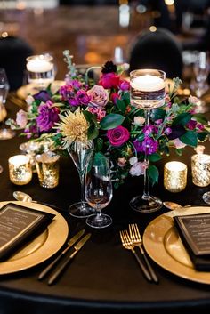 the table is set with gold plates and place settings, flowers in glass vases